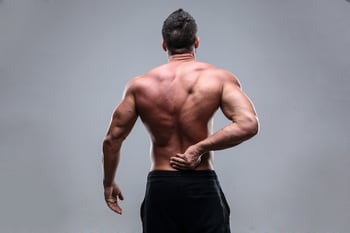 Muscular man with back pain on a gray background