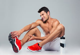 Portrait of a fitness man with foot pain over gray background